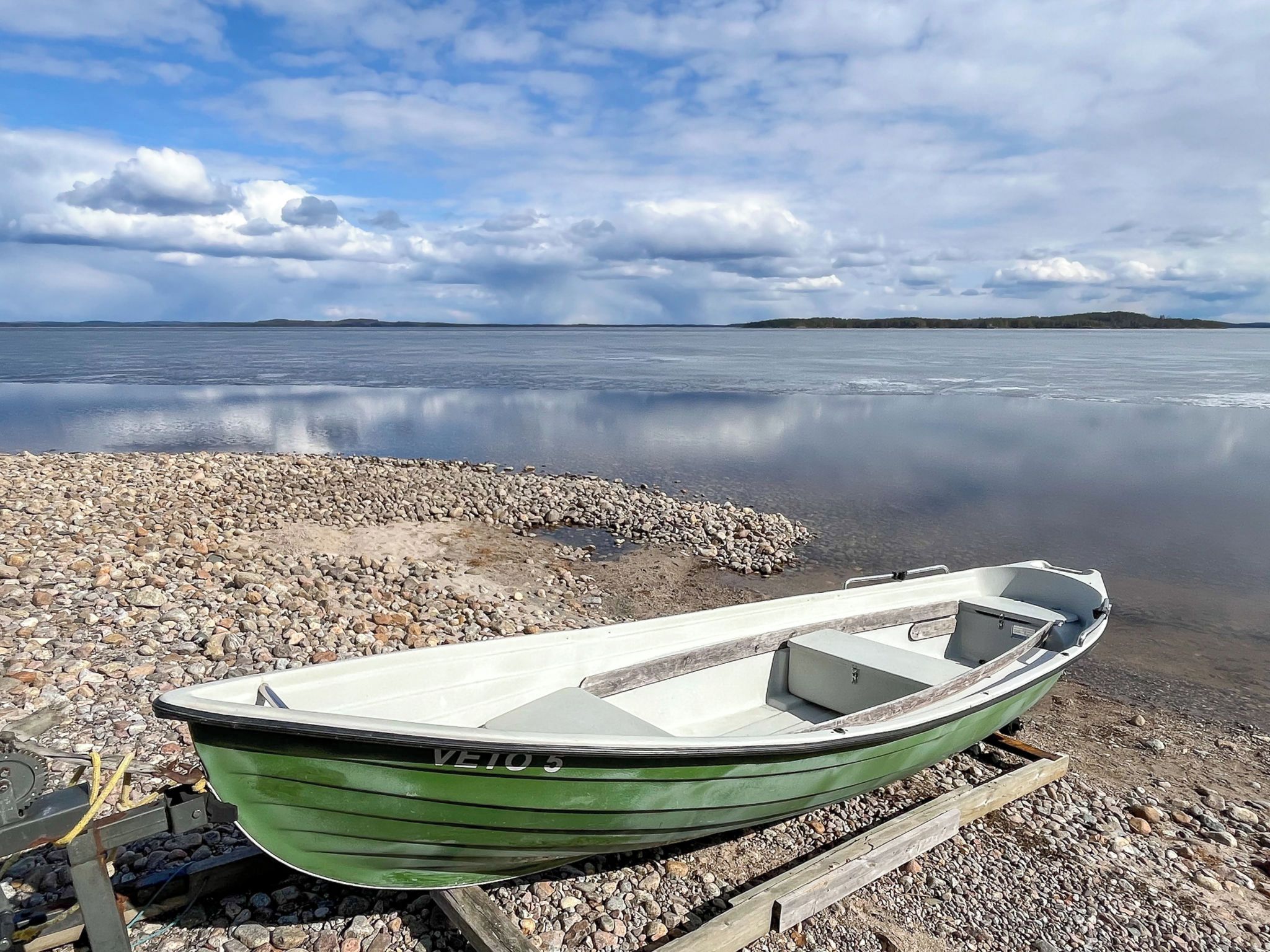 Ein grünes Boot an einer felsigen Küste, ruhiges Wasser und ein bewölkter Himmel.