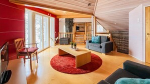 Een moderne woonkamer met een houten plafond, een rode accentmuur, een groot raam en een trap naar een hoger niveau.