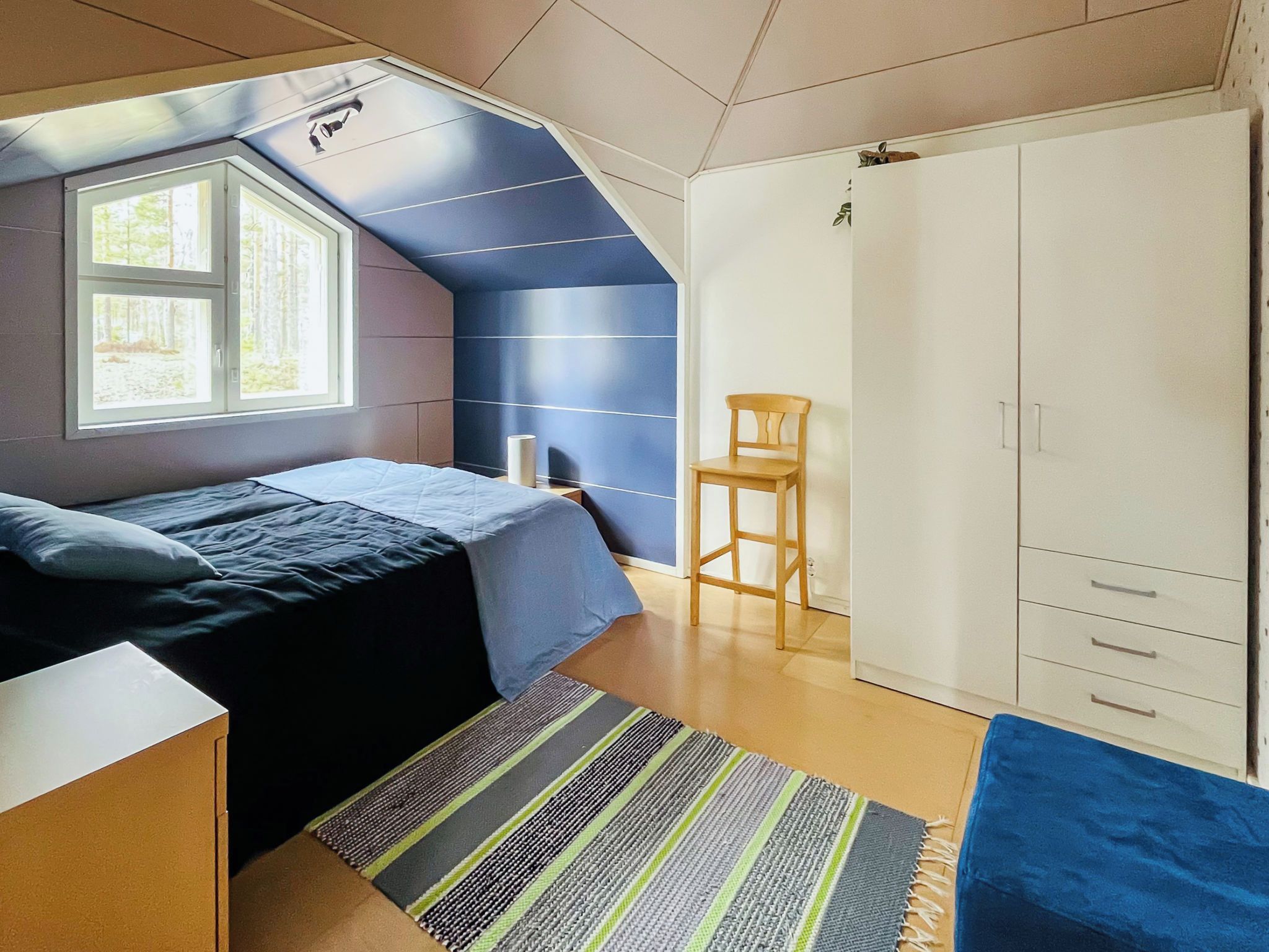 A bedroom with a bed, a chair, a wardrobe, and a window.