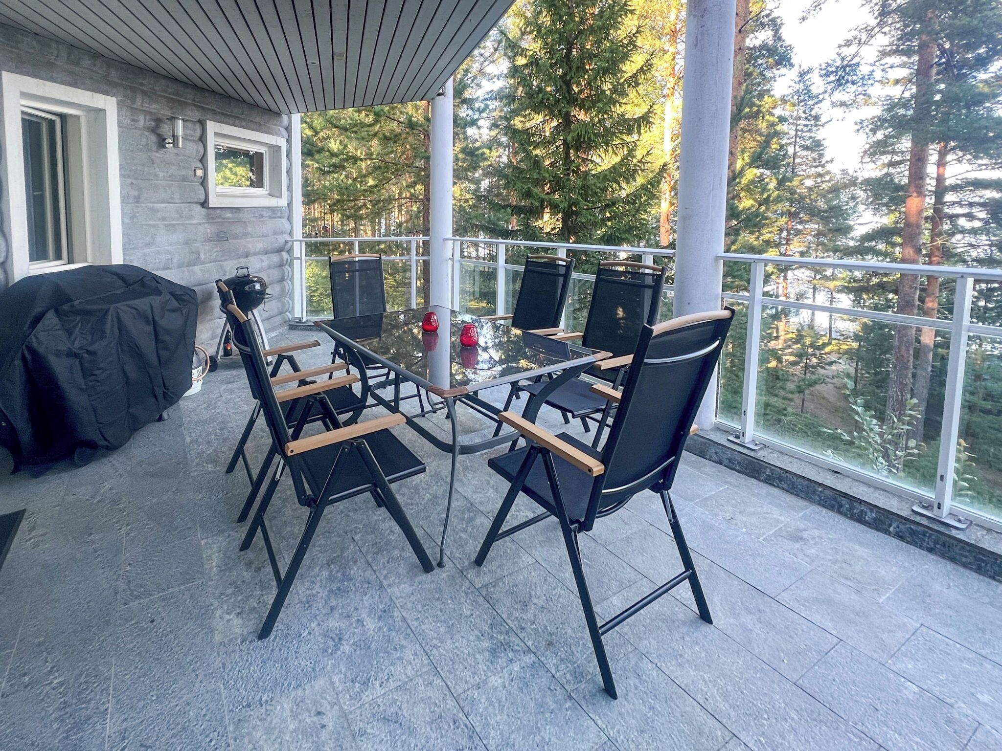 Eine überdachte Terrasse im Freien mit Tisch und Stühlen, einem Grill und Blick auf Bäume.