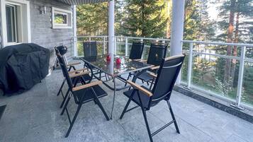 Eine überdachte Terrasse im Freien mit Tisch und Stühlen, einem Grill und Blick auf Bäume.