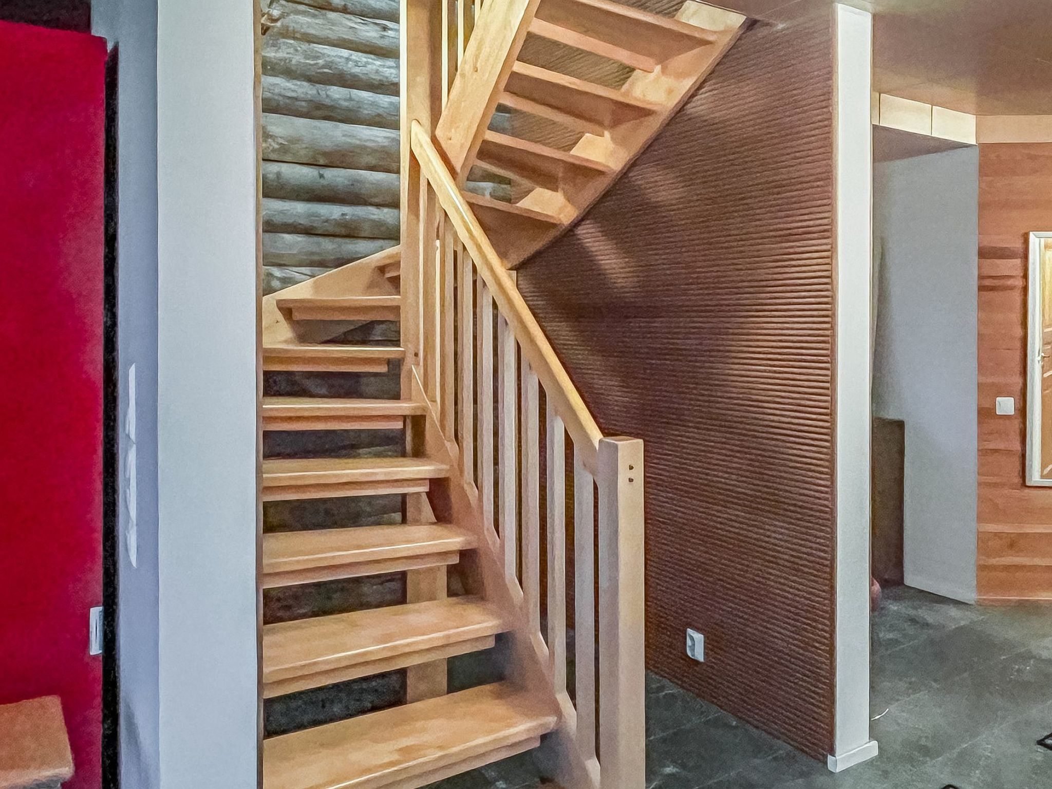 Eine Holztreppe mit Handlauf, die zu einem Raum mit strukturierter Wand führt.