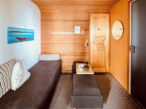 A small, cozy room with two single beds, a wooden wall, a door with a circular handle, and a small table with a plant.