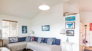 Quarto com duas camas, uma mesa e uma luminária. Há quadros na parede e uma janela com persianas.