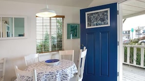 Uma área de refeições com mesa e cadeiras, uma janela com persianas e uma porta azul com um quadro emoldurado.