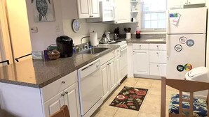 A kitchen with white cabinets, a granite countertop, a coffee maker, and a refrigerator with magnets.