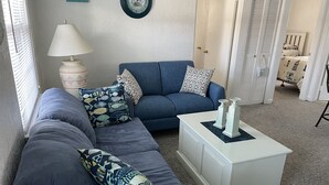 A living room with a blue sofa, patterned pillows, a white side table, and a clock on the wall.