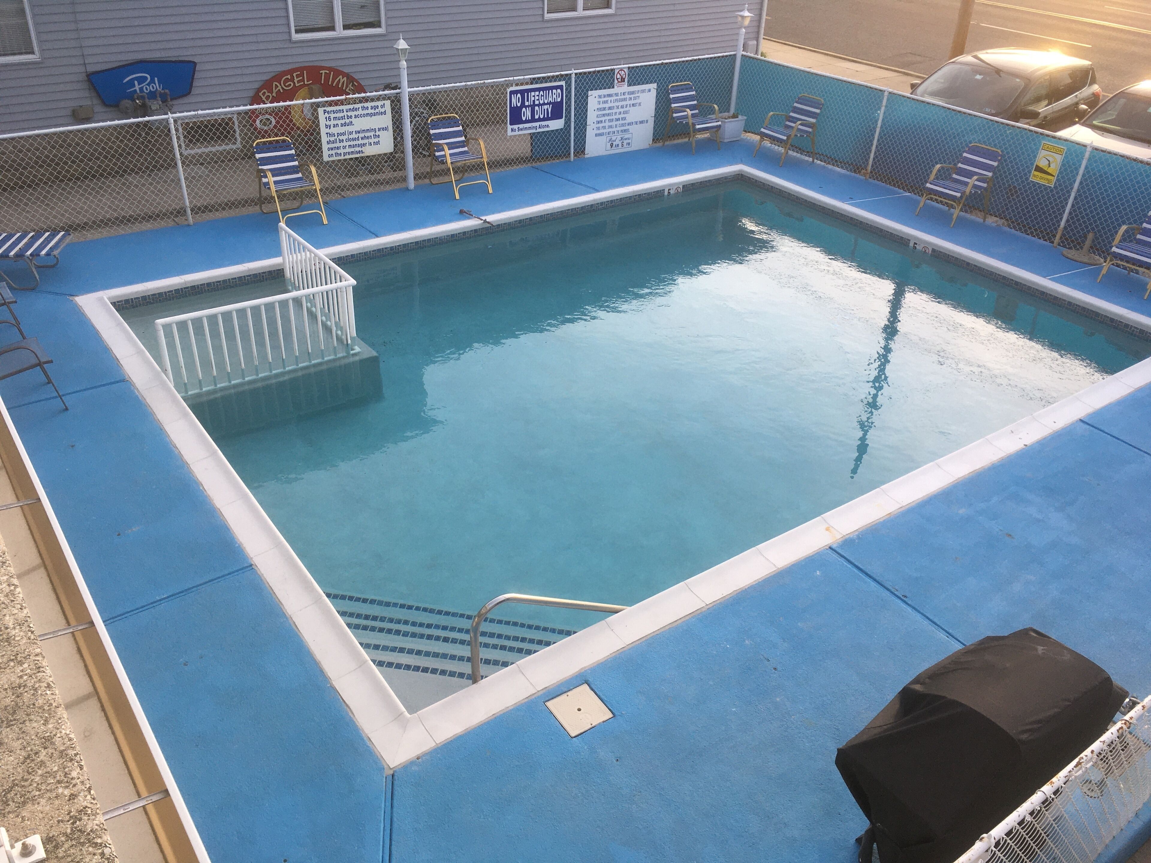 Une piscine rectangulaire dont le bord est recouvert de carreaux bleus, avec une échelle blanche et quelques chaises longues.