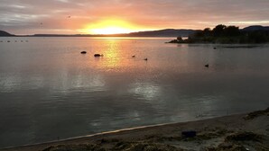 Ein Sonnenuntergang über einem ruhigen See mit Booten und einer entfernten Uferlinie.