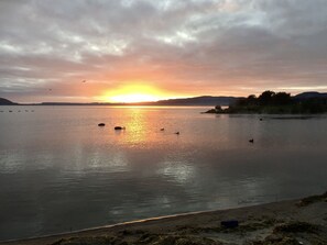 A sunset over a calm lake with boats and a distant shoreline.