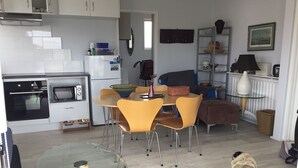 Una cucina moderna con mobili bianchi, un forno integrato e un forno a microonde. C'è un'area pranzo con un tavolo in vetro e sedie gialle. Si vede un cagnolino pug in primo piano.