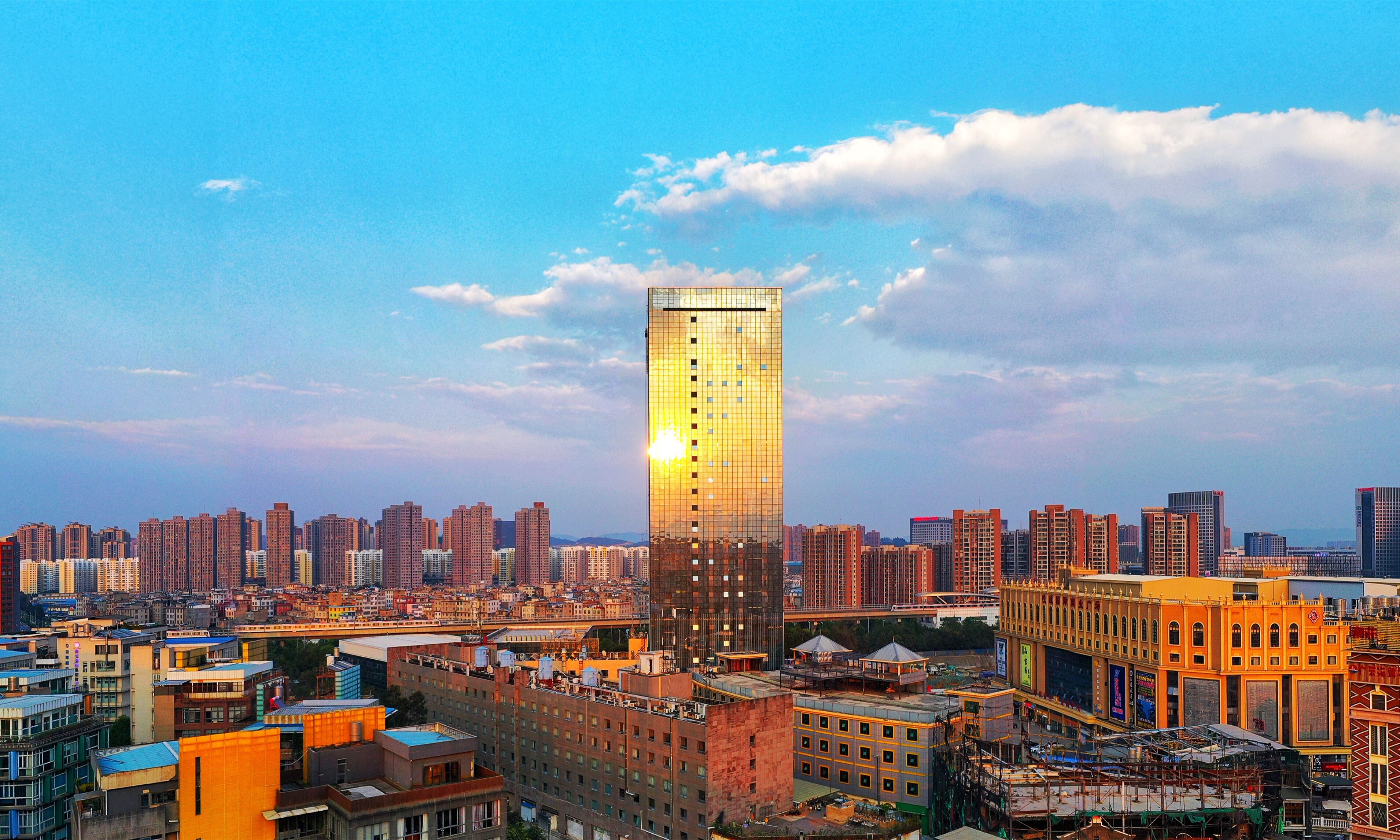 Un edificio de gran altura con fachada de vidrio reflectante, rodeado por una zona urbana densa y varios otros edificios.