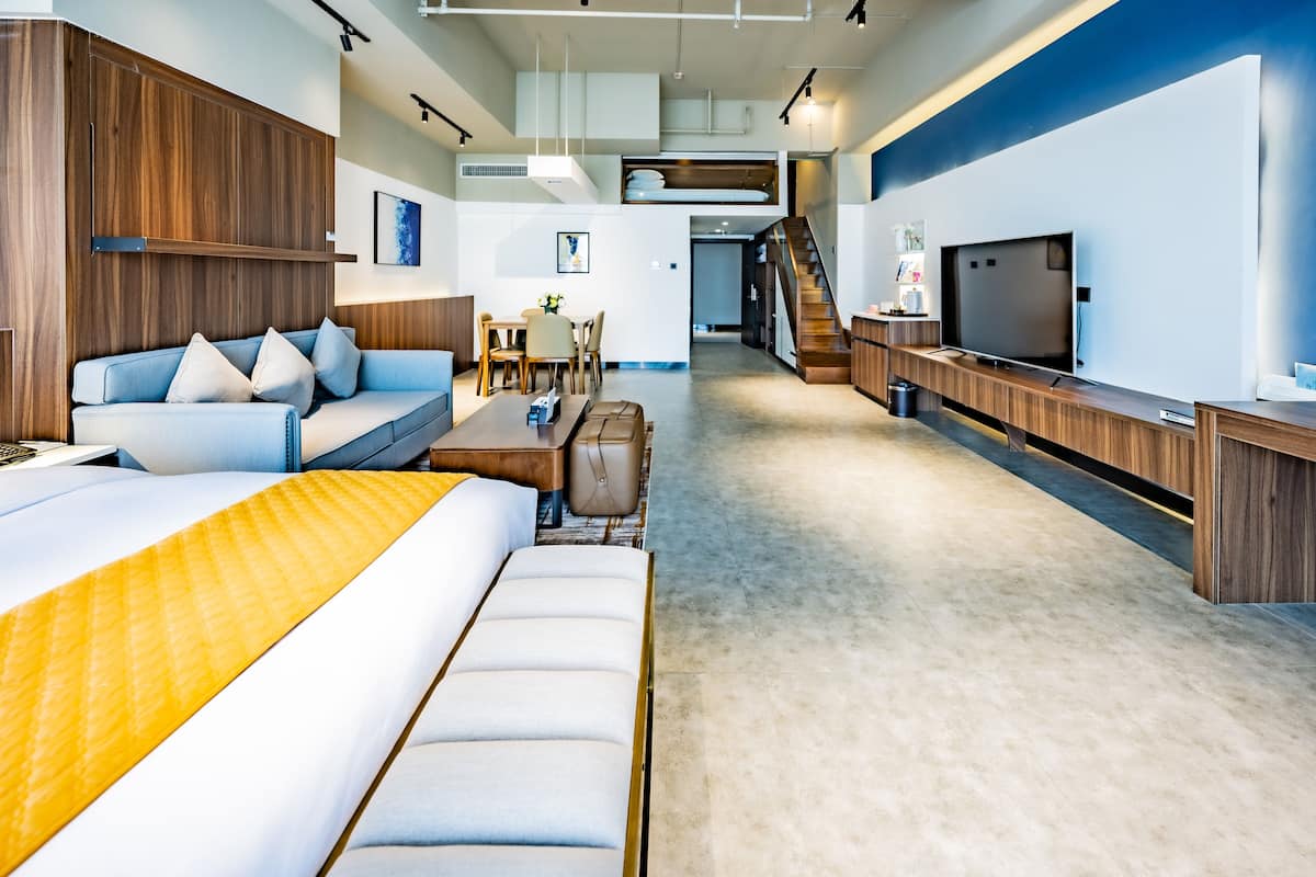 A modern hotel room with a sofa, a bed, a desk, a TV, and a staircase.