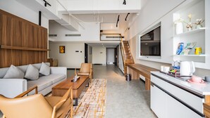 Un intérieur moderne comprenant un canapé, des fauteuils, une table en bois, un coin cuisine et un escalier.