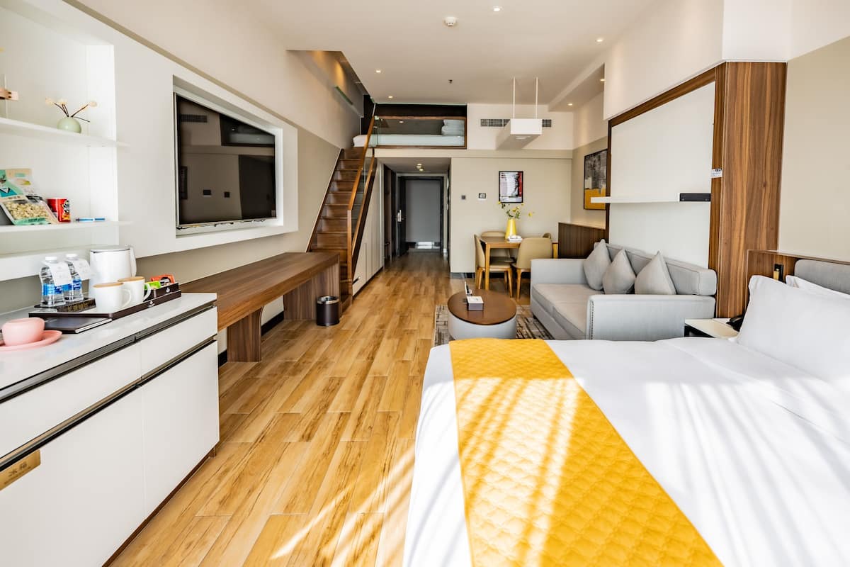 A modern hotel room with a bed, a sofa, a desk, and a staircase leading to an upper level.
