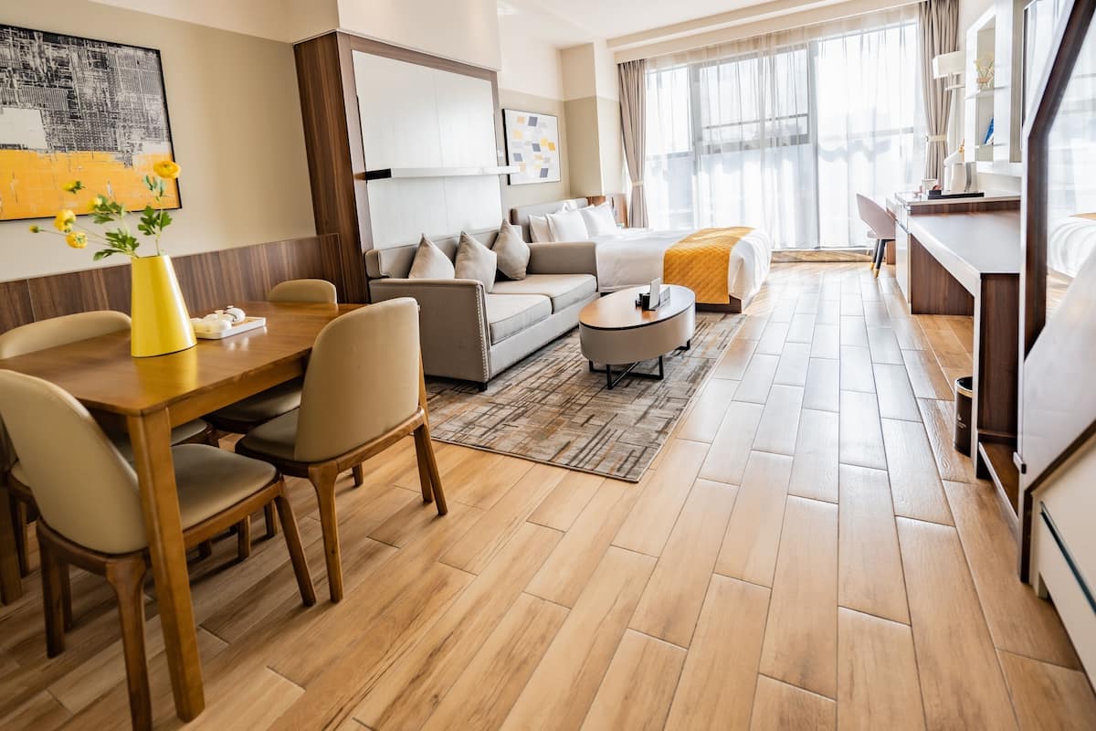 A modern hotel room with a dining area, a sofa, a bed, and a large window.