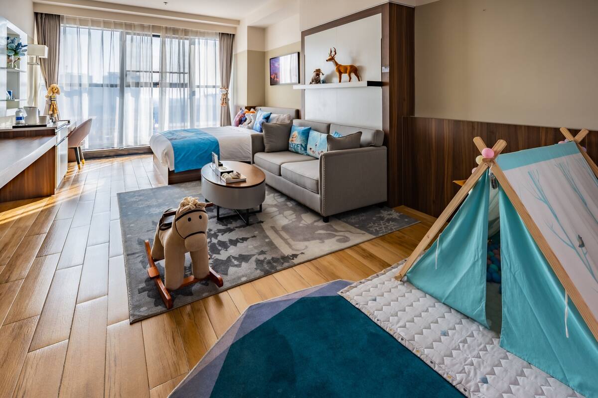 A modern hotel room with a bed, sofa, desk, and a tent-like play area.