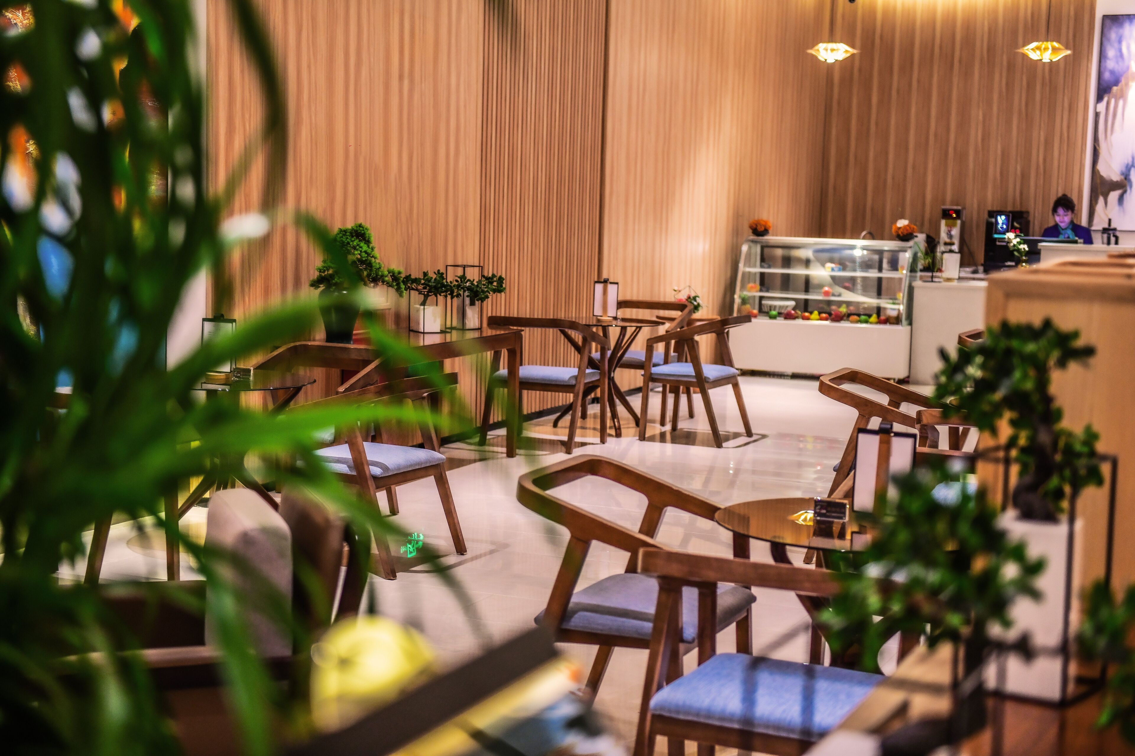 Un vestíbulo moderno de hotel con mobiliario de madera, una vitrina con frutas y un mostrador de recepción.