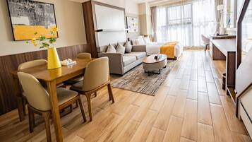 A modern hotel room with a dining area, a sofa set, and a large window.