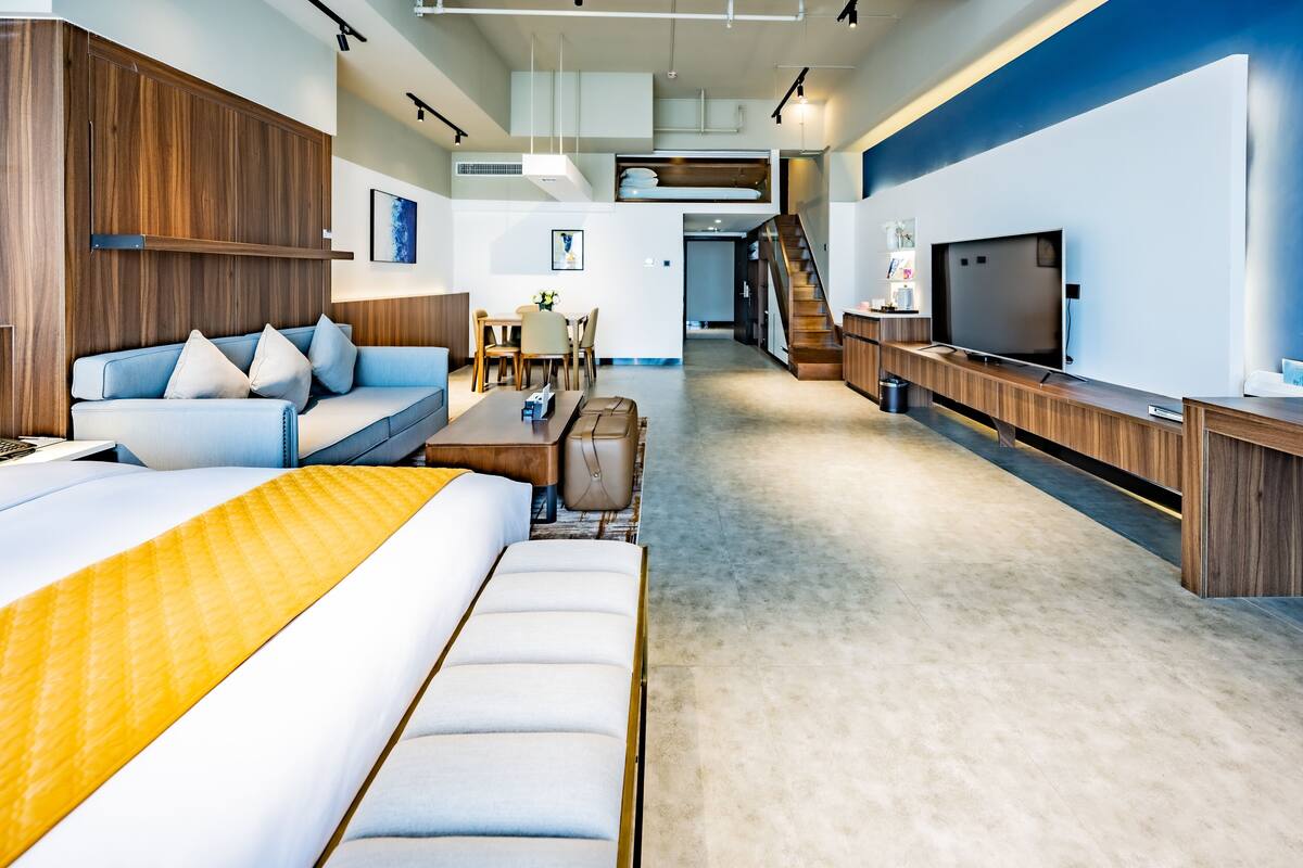 A modern hotel room with a sofa, a bed, a desk, a TV, and a staircase.