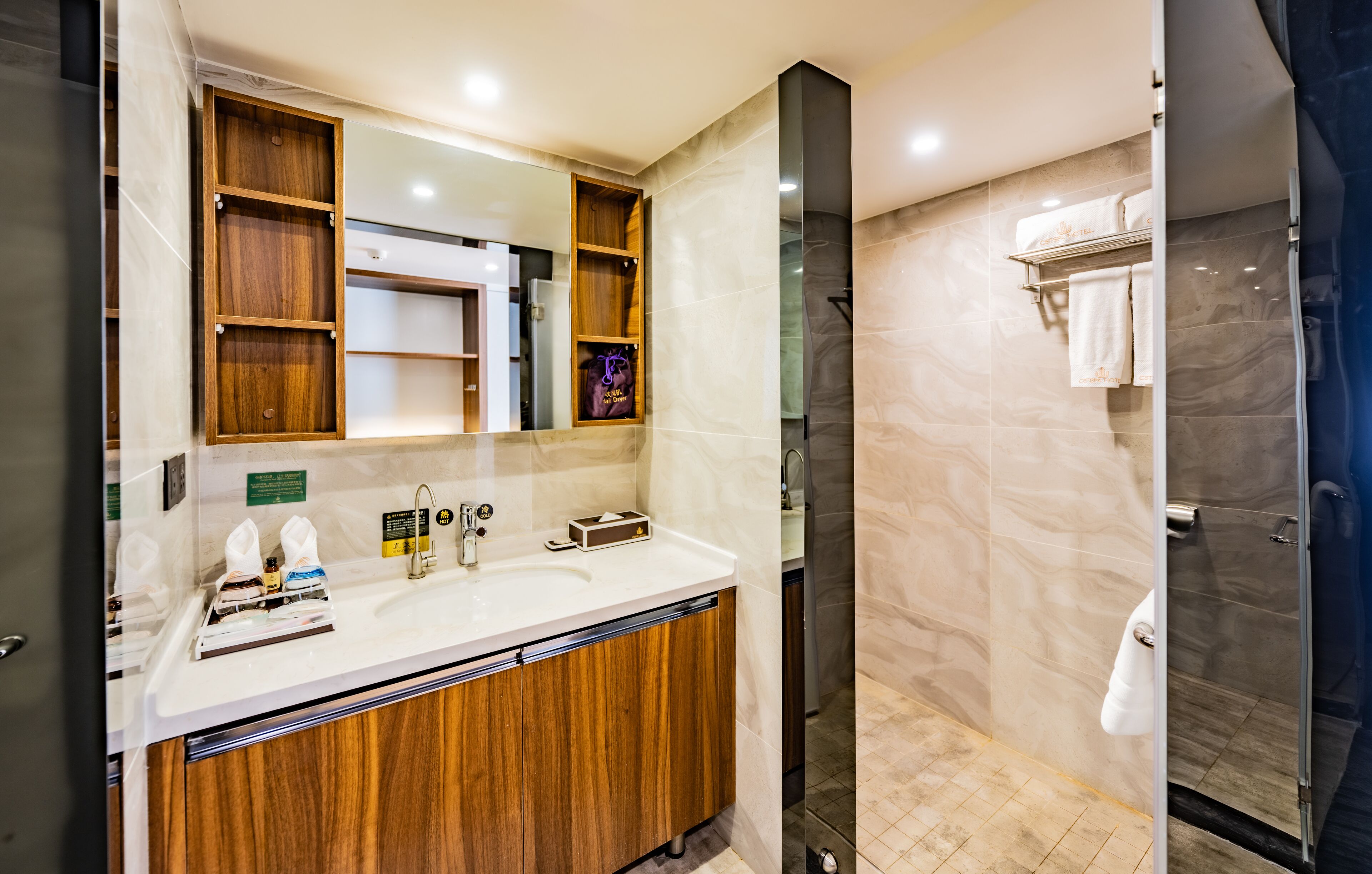A modern bathroom with a wooden vanity, a large mirror, and a glass shower enclosure.