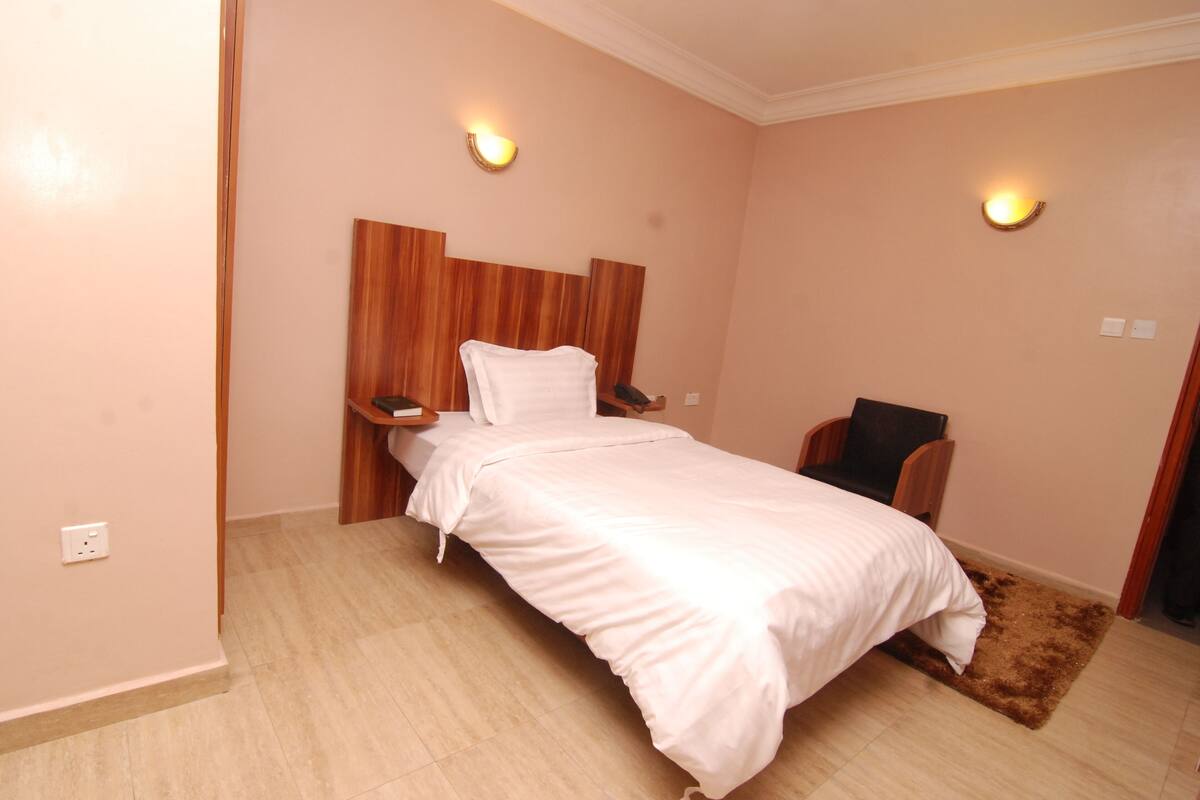 Uma cama bem arrumada com cabeceira de madeira, duas mesas de cabeceira e uma pequena cadeira.