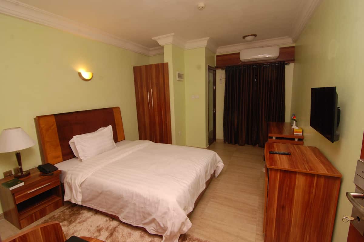Quarto de hotel com uma cama grande, uma escrivaninha com cadeira, televisão e guarda-roupa.
