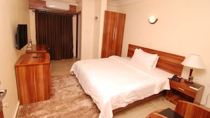 A hotel room with a large bed, a wooden desk, a television, and a wardrobe. - Fisher Suites and Apartments (Abuja)