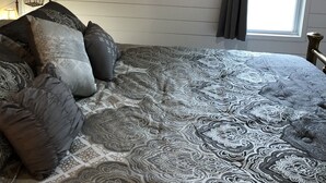Une chambre à coucher avec un grand lit, un plafond en bois, un miroir, une fenêtre et une table de chevet avec une lampe.