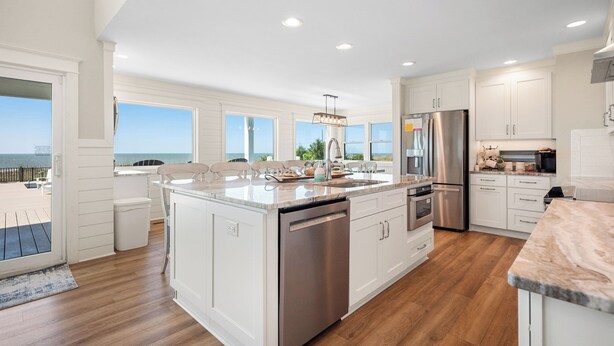 A modern kitchen with white cabinetry, a stainless steel refrigerator, and a large island with a dishwasher. - Serenity by the Sea: Nostalgic Oceanfront Home with Room for the Whole Family (Oak Island)