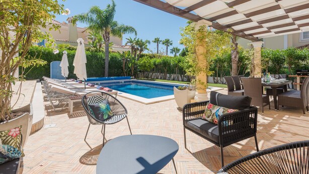 Ein Poolbereich mit Liegestühlen, einem Tisch und einer Pergola.