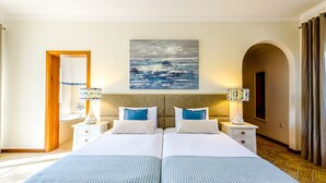 Ein Hotelzimmer mit zwei Betten, einem Meeresbild an der Wand und Blick auf das Meer durch einen Bogen.