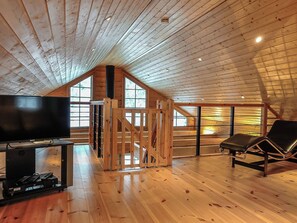 Une pièce mansardée spacieuse, avec un plancher en bois, une télévision et un fauteuil.