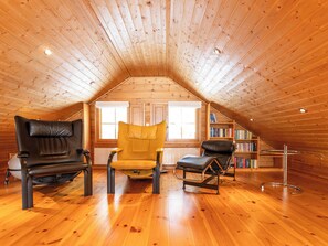 Une pièce mansardée chaleureuse avec des lambris en bois au plafond, une bibliothèque et trois fauteuils en cuir.