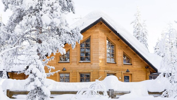 Una cabaña de madera con varias ventanas y techo inclinado, rodeada de árboles cubiertos de nieve.
