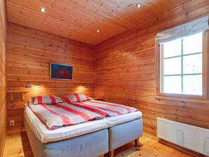 Une chambre dans une cabane en bois, avec un lit, une fenêtre et un tableau accroché au mur.