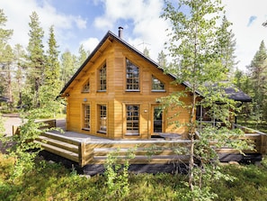 Une cabane en bois à deux étages, dotée d’une terrasse et entourée d’arbres.