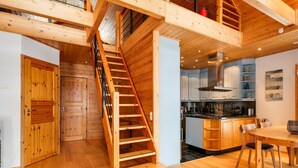 Interior de madera con una escalera que conduce a un altillo, una cocina con electrodomésticos modernos y un comedor con mobiliario de madera.