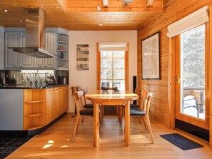 Une cuisine moderne avec des meubles en bois, une hotte en acier inoxydable et un coin repas comprenant une table et des chaises en bois.