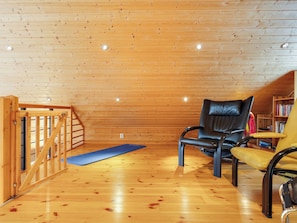 Un intérieur en bois avec un fauteuil en cuir noir, une chaise jaune et un tapis bleu sur le sol.