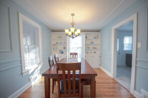 A dining area with a wooden table and chairs, a chandelier, and built-in shelving with kitchen items.