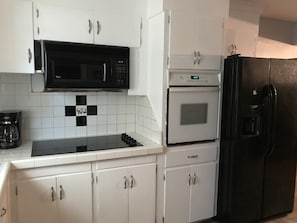 A kitchen with white cabinets, a black microwave, a white oven, and a black refrigerator.