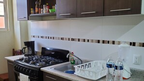 Una cucina con mobili impiallacciati in legno scuro, un fornello a gas, un lavandino e un piano di lavoro con due bottiglie d'acqua.