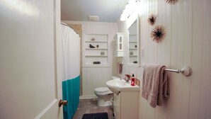 Une salle de bain équipée de toilettes, d’un lavabo et d’étagères où sont rangés les articles de toilette.