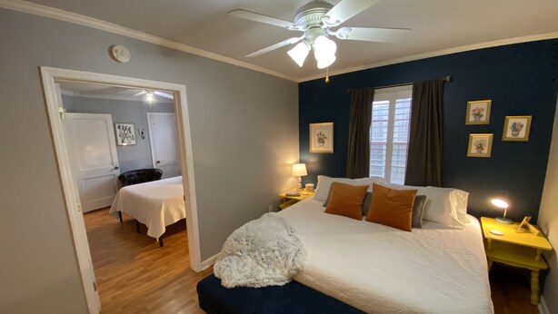 Une chambre à coucher avec un lit, des tables de chevet, un ventilateur de plafond et une fenêtre avec des rideaux.