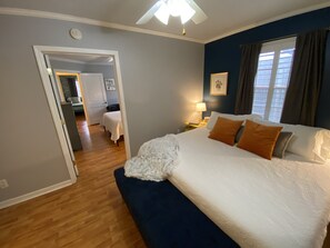 Une chambre à coucher avec un grand lit, une table de chevet avec une lampe, une fenêtre avec des rideaux et une porte donnant sur une autre pièce.