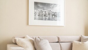 A beige sofa with multiple cushions against a wall, above which is a framed black and white photograph of buildings. - Santa Fosca Design Apartment R&R (Venecia)