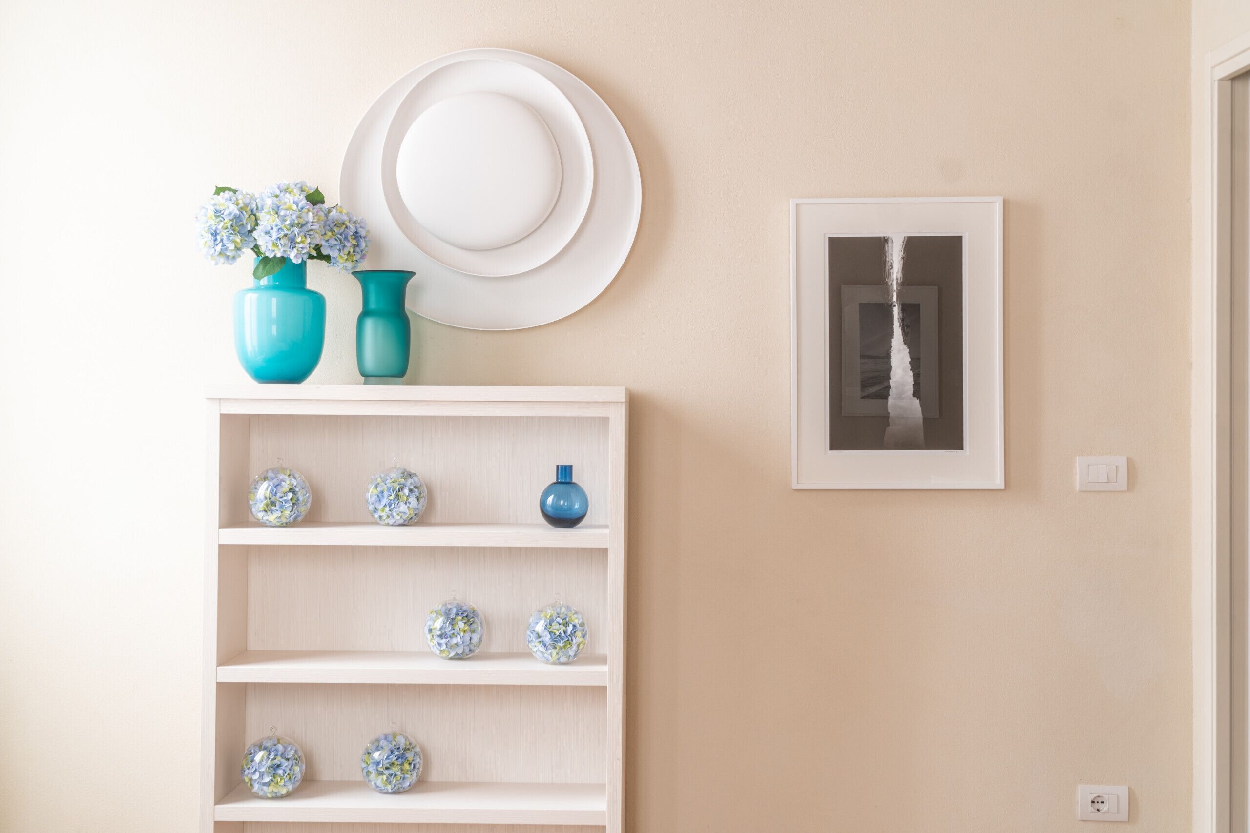 A wall with a white shelf holding decorative items, a white hat, and a framed picture.