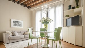 A modern living room with a sofa, a dining table with chairs, a chandelier, and a television on a cabinet. - Santa Fosca Design Apartment R&R (Venecia)