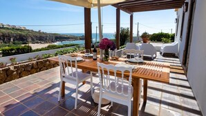 A terrace with a wooden table, white chairs, a tablecloth, and a vase of flowers. - Villa S. Lourenço by ACasaDasCasas (Ericeira)